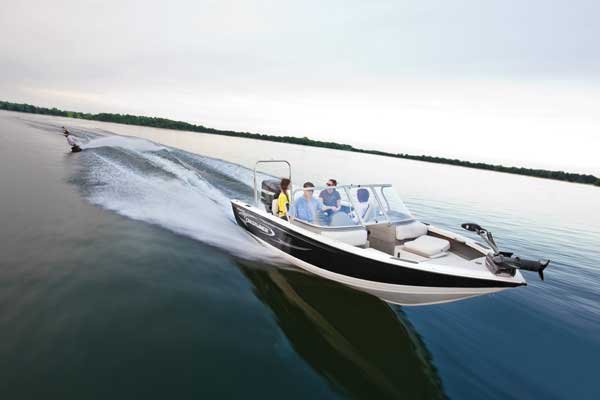 Panoramic view of four people riding a powerboat during daytime, while another person is water skiing