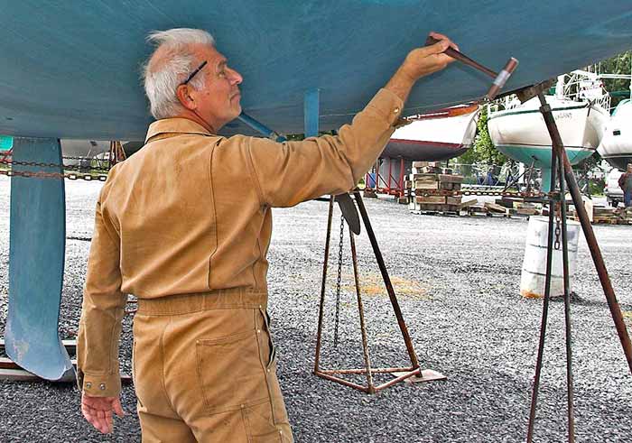 Older man testing the hull of a boat on jackstands