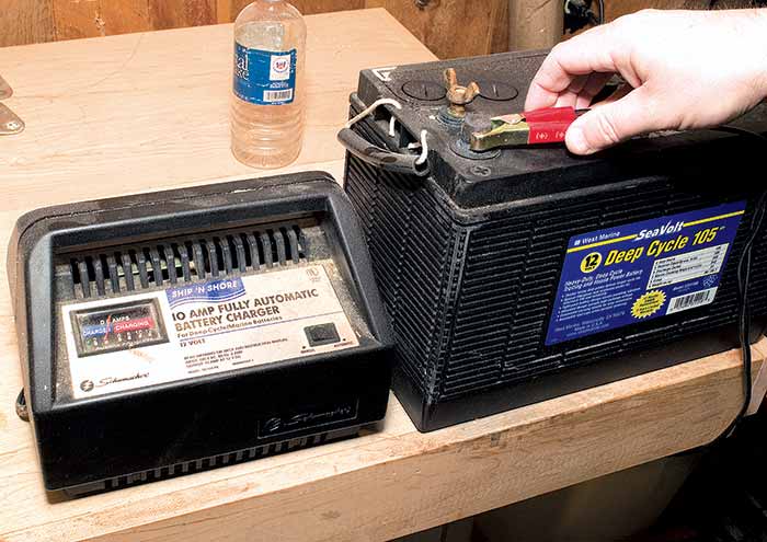 A person places a red clamp on a car battery