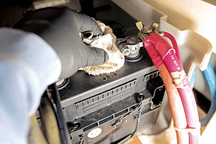 A hand is cleaning a battery terminal with a white cloth