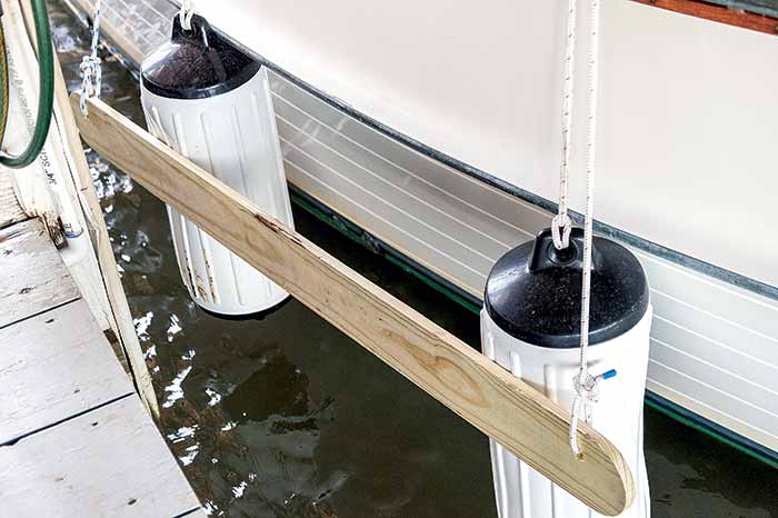 Wooden board with holes on each ended with rope going through them against boat fenders