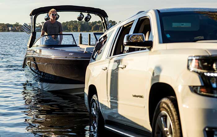 SUV towing small powerboat up ramp with man in powerboat standing at the helm