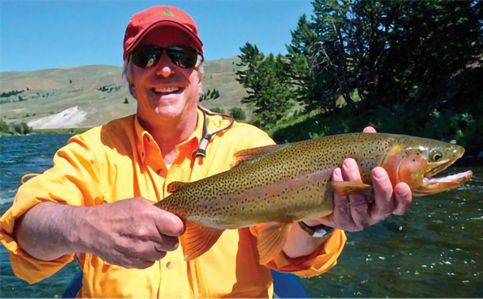 Actor Henry Winkler wearing a yellow shirt, red ball cap and sunglasses holds up a trout he just caught