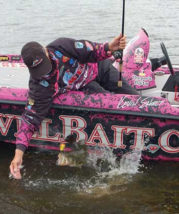 A fishermen leaning over the side of his bright pink boat holding a fishing pole