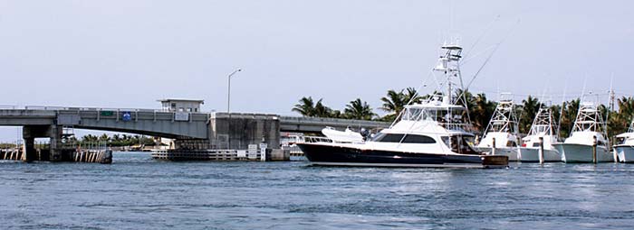 Large blue and white powerboat crusing towards drawbridge with other large powerboats docked in the background