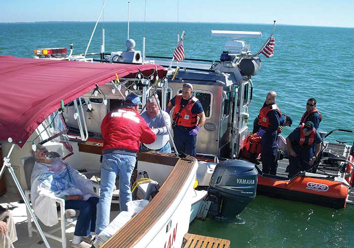 A coast guard boat and two other boats are rafted up together, a man with a brigh red jacket is handing something to another man in a boat