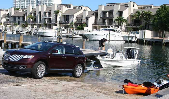 SUV launching small powerboat at boat ramp with orange kayak nearby