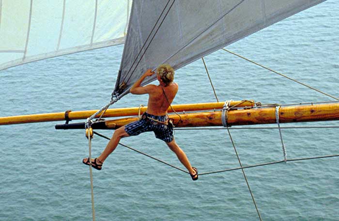 Man standing aloft in in sailboat rigging setting a sail
