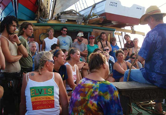 Man in a straw hat demonstrating splicing a rope on a boat deck infront of a group of people