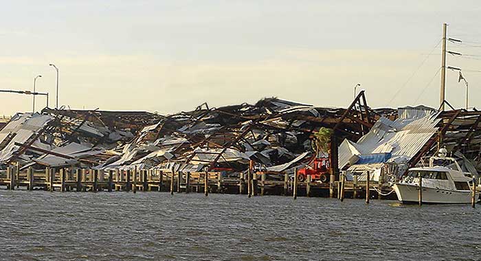 A white powerboat is safely docked in the water next to a large metal structure on land that has fallen, it is filled with smaller boats