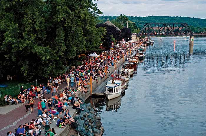 Aerial view of a large group of men and women of various ages sitting on the dock of a marina surrounded by small boats