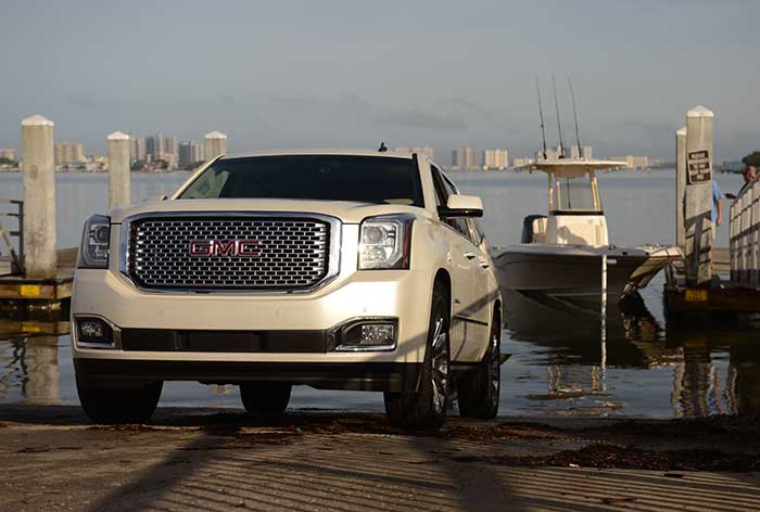 Beige GMC SUV backing down a boat ramp with a powerboat floating behind it