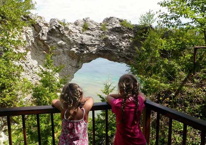 Two young girls standing along a railing view Arch Rock on Mackinac Island.