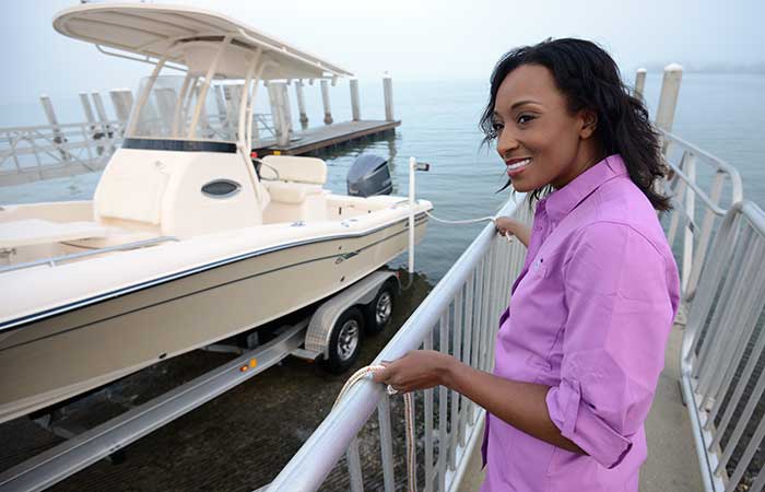 Woman wearing a purple shirt standing on a floating dock watch as a powerboat on a boat trailer backing into the water