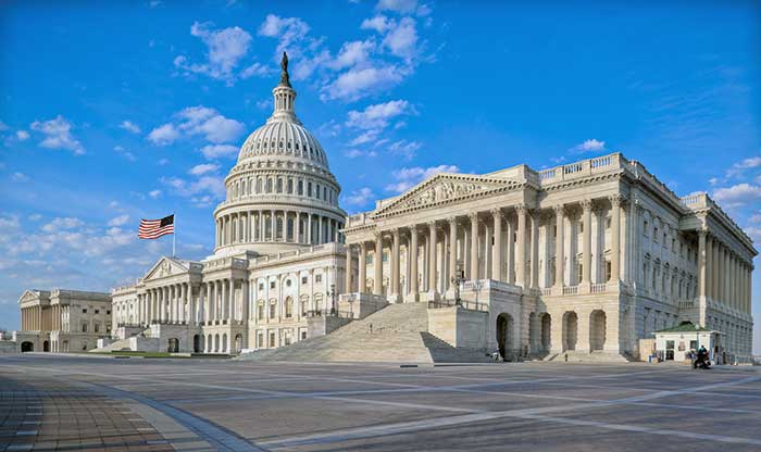 U.S. Capitol building in a side view under a bright blue sky with a few wispy clouds