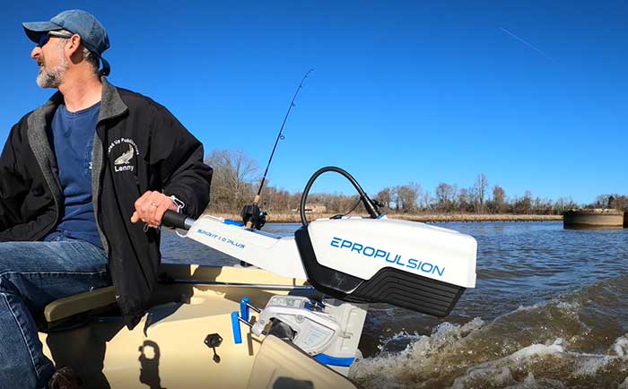 Man sitting in small fishing boat with hand on the tiller of an electric trolling motor crusing through the water