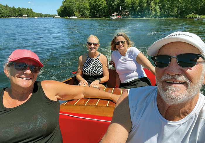 A man at the helm cruising with three women aboard a wooden runabout boat