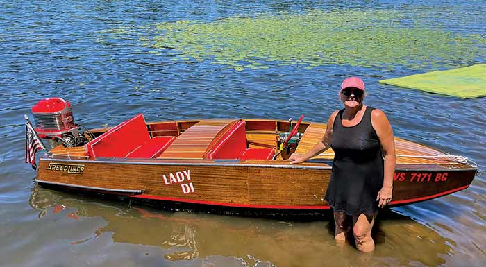 Man standing by the water with his wooden outboard runabout boat
