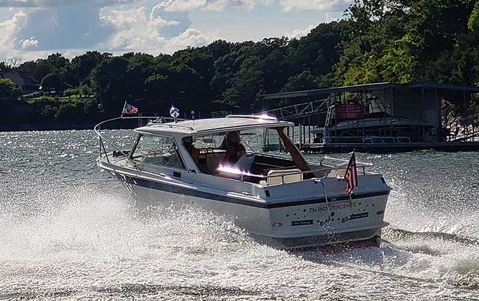 Rear view of a renovated Uniflite 23 Sport Fisherman Hardtop powerboat cruising along a lake