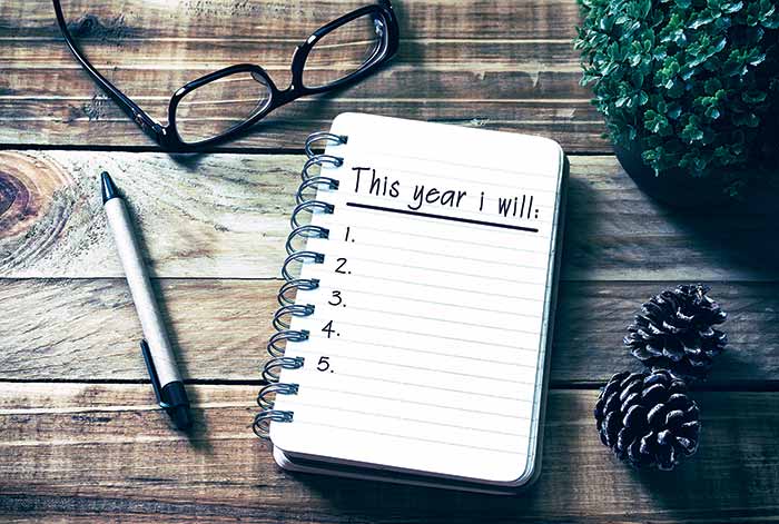 Spiral-bound notebook lies open with pen, eye glasses, greenery and pine cones on a wooden table
