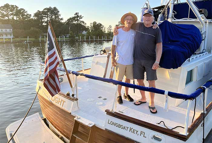 Two men standing on the bow of a Grand Banks 42 trawler tied to a dock with the sun streaming over them