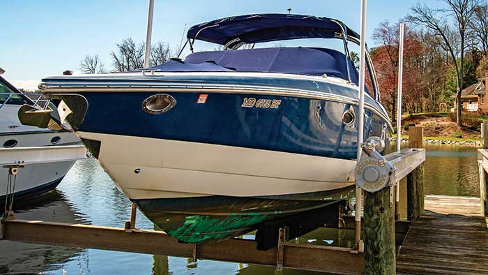 Large blue and white powerboat sitting on a boat lift with water and trees in the background