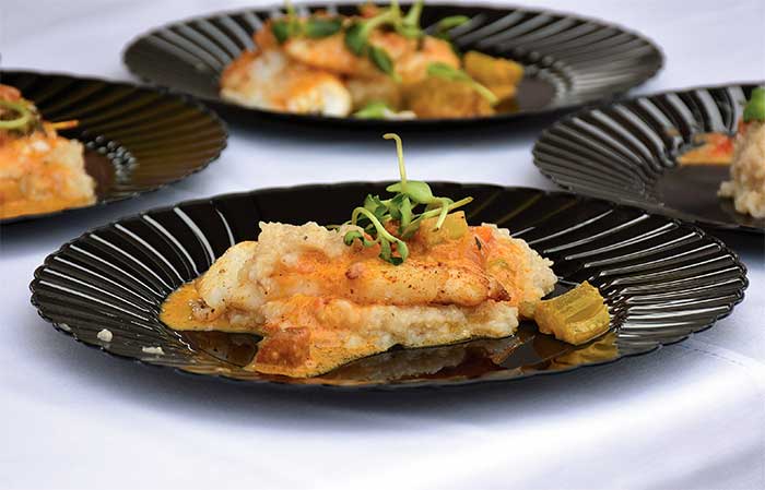 Four cooked black plates of lionfish fillets on mashed potatoes with sauce pieces of okcra and green herb garish