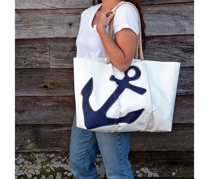 Adult female in a white t-shirt, blue jeans and a large white sea bag featuring a navy anchor.