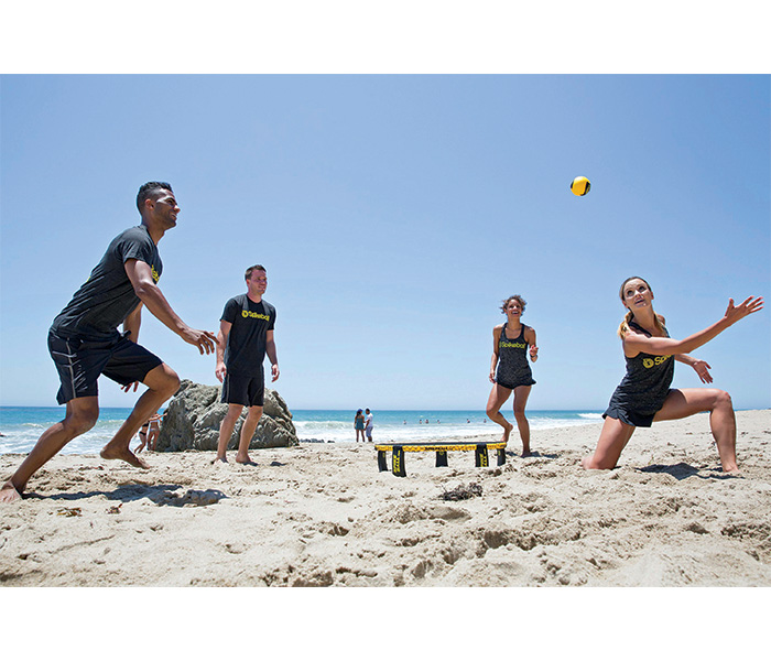 Two adult males and two adult females playing a game on the beach during a sunny day.