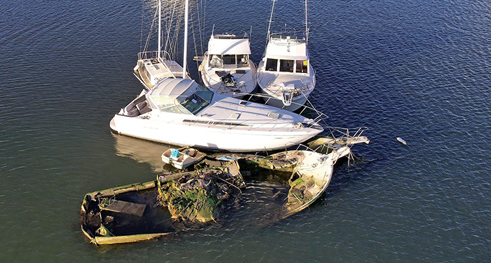 Three white derelict vessels surround a discarded sunken wreak in open waters.