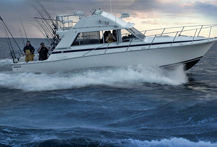 Large white vessel with several fisherman on the open waters at sunset.