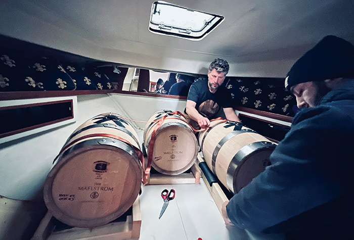Two men securing three barrels inside the cabin on a boat.