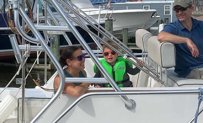 Woman kneeling and toddler standing at the side with man sitting at the helm of a powerboat