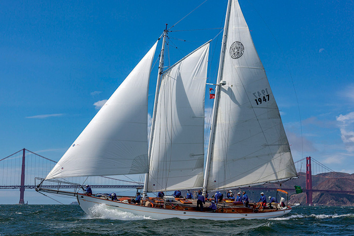 Large white sailboat with three white sails sailing by the Golden Gate Bridge