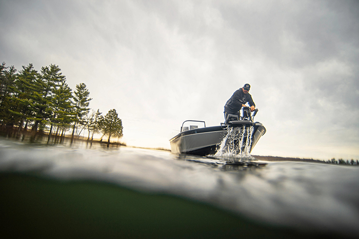 Adult male wearing a black hat and black hoodie pulling in a trolling motor on the front of a boat.