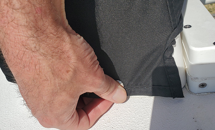 A hand holding down silver snaps on a white boat's black cover.
