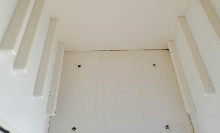 Inside of an empty white tacklebox with holes drilled for mounting screws.