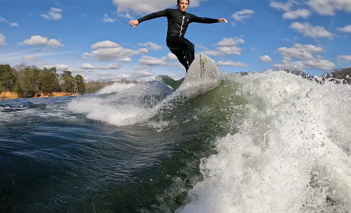 Young adult male in a black wet suit wakeboarding.