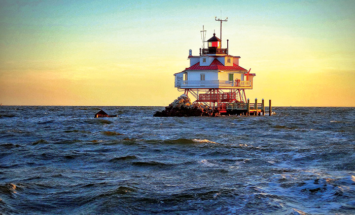 A  view of a white and red lighthouse during sunset from blue waters.