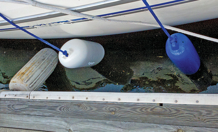 A white and blue cylindrical fenders protecting a white boat next to a wooden dock. 