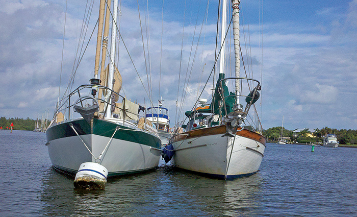 Two white sailboats next to each other on open waters and protected by a rafting cushions.
