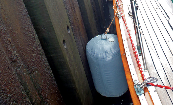 A vertically hung gray fender providing protection for a vessel next to a lock wall. 