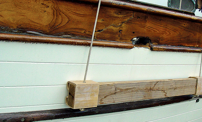  A wooden fender board positioned on the side of a white vessel.