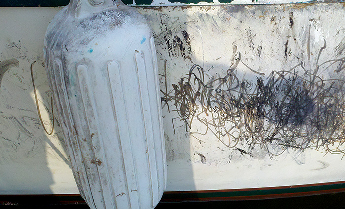 Up close view of damaged damaging gelcoat on the side of a white boat.