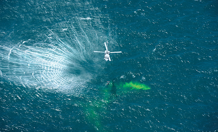 Ariel photo of a white rescue helicopter during a rescue over blue open waters.