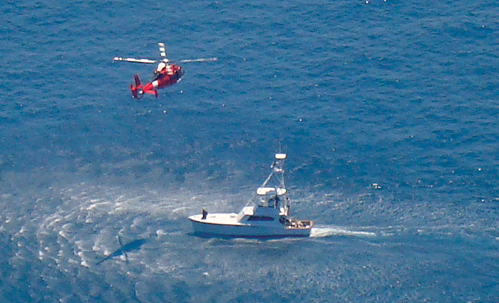 Rescue helicopter approaching a white vessel in open waters on a clear day.