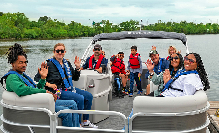 Mixture of adults and kids waving as they enjoy a pontoon boat ride during a partly cloudy day.