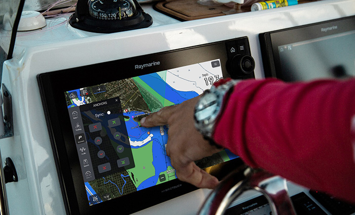 Close-up photo of an adult hand using a touch screen navigation system on a boat.