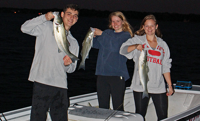 An adult male and two adult females proudly displaying three fish caught during night fishing.