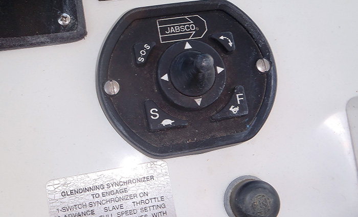 Black mounted control for boat spotlights on the dash of a white vessel.